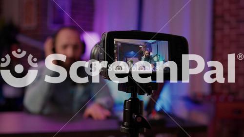 Selective Focus On Digital Video Camera Screen Recording Male Vlogger With Headphones Talking At Microphone In Home Podcasting Studio. Closeup Of Dslr Filming Influencer Streaming Live Internet Show.